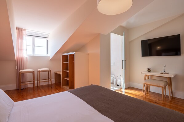 A modern hotel room with a large bed, two wooden chairs, a desk, a wardrobe, and a TV mounted on the wall.