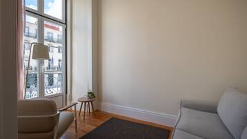 A modern living room with a large window, a sofa, a small table with a plant, and a lamp.