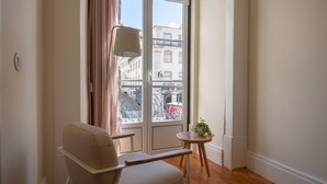 Una habitación con un ventanal grande, una silla, una mesita y una planta en maceta.
