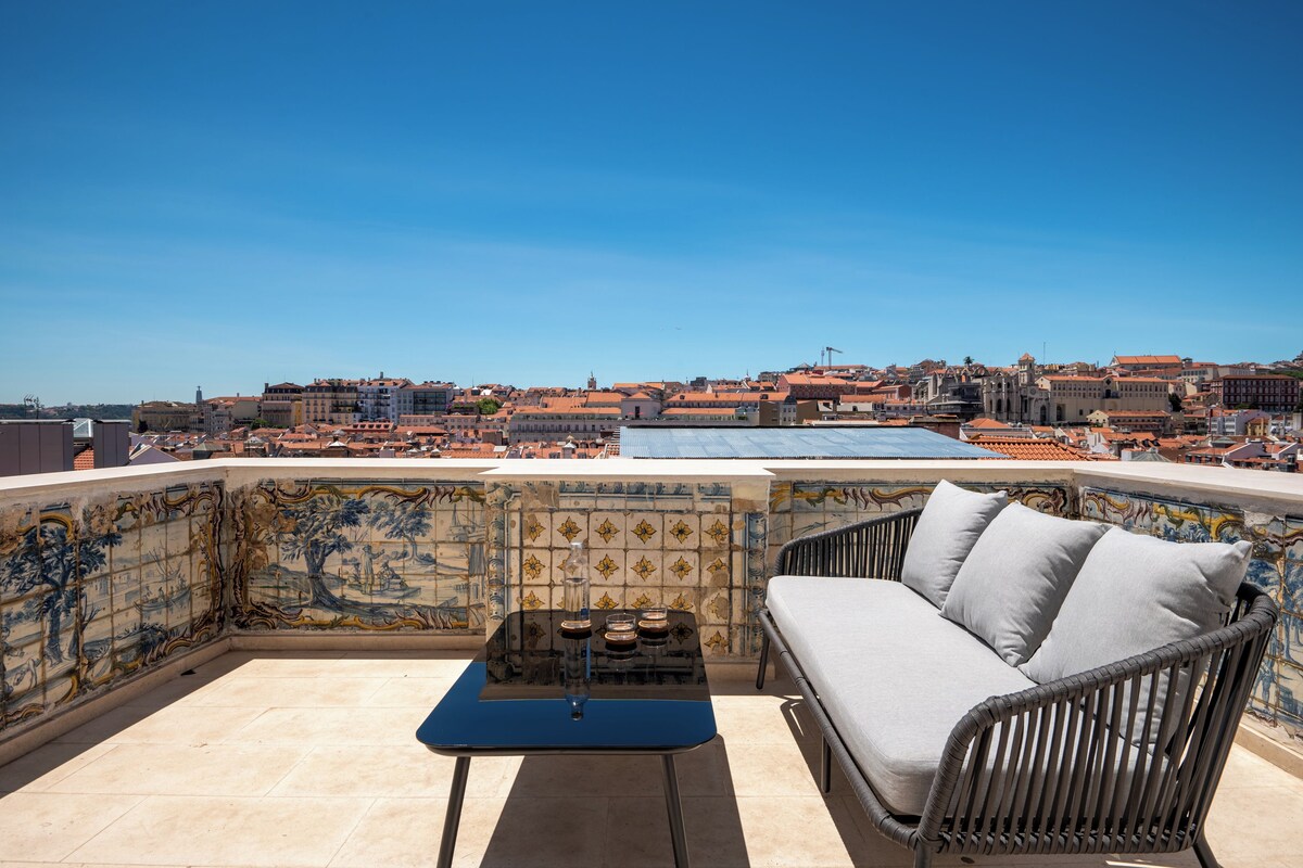 Eine Dachterrasse mit Korbsessel, kleinem Tisch und einer Wand mit Mosaikgestaltung.