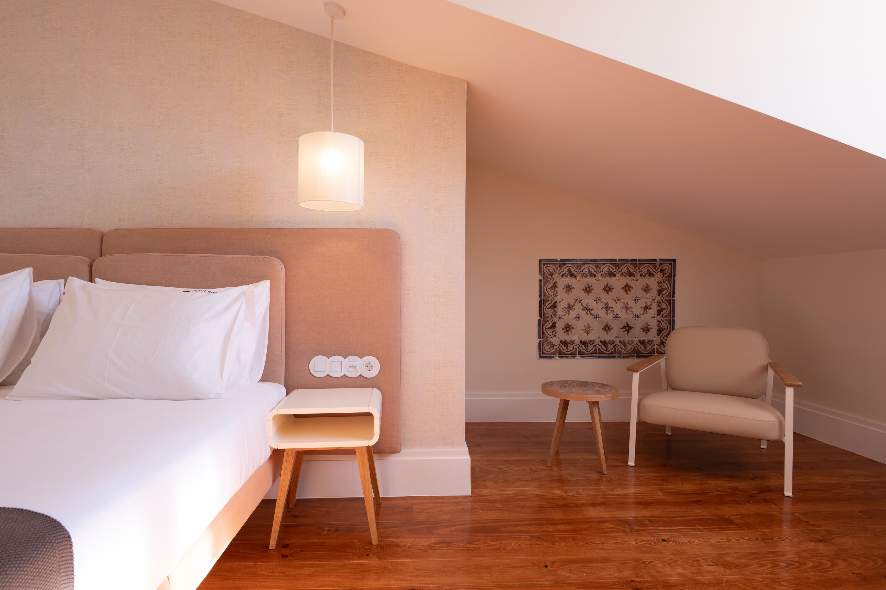 A bedroom with a bed, bedside table, lamp, chair, and a decorative wall piece.