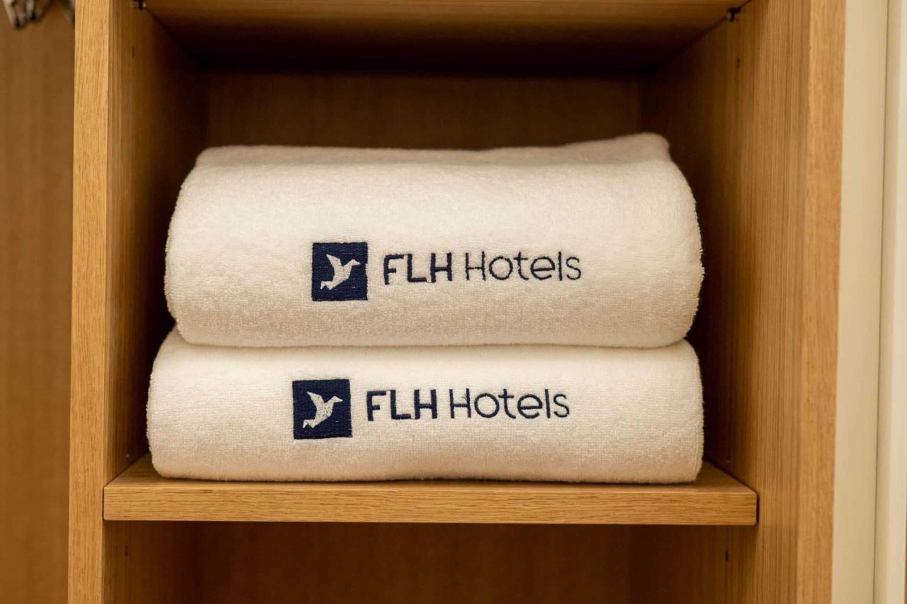 Twee gevouwen handdoeken met het logo van FLH Hotels in een houten kast.