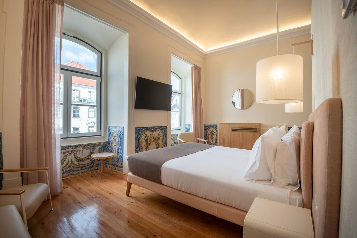 Habitación de hotel con una cama grande, televisión, una mesita redonda y una ventana con cortinas.