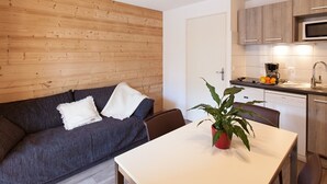 Un espacio habitable moderno con un revestimiento de pared de madera, un sofá gris oscuro con cojines blancos, una mesa blanca y una planta en maceta roja.