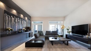 A modern living room with a sectional sofa, a flat-screen TV, and a large abstract painting on the wall. - Maison Privee - Luxurious 2/Bed Apt on Palm Jumeirah (Dubai)