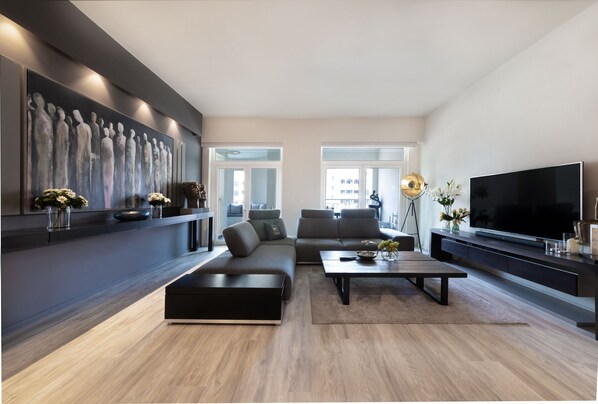 A modern living room with a sectional sofa, a flat-screen TV, and a large abstract painting on the wall.