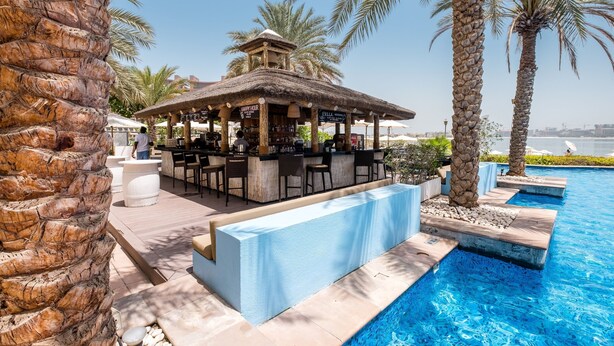 A poolside bar area with a thatched roof, seating, and a view of the pool. - Maison Privee - Luxurious 2/Bed Apt on Palm Jumeirah (Dubai)