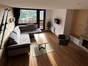 A modern living room with a sectional sofa, a coffee table, a fireplace, and a TV mounted on the wall.