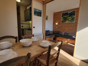 A dining area with a wooden table set for four, a sofa, and a kitchen in the background.