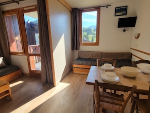 A cozy room with a wooden table set for dining, a bench with cushions, and a view of the outdoors through a large window.