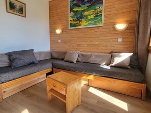 A modern living room with a wooden sectional sofa, a wooden coffee table, and two wall-mounted light fixtures. - Functional divisible studio · Direct slope access · Pets allowed (Belle Plagne)