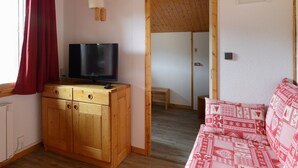 Una habitación acogedora con un armario de madera, un televisor, un sofá rojo estampado y techo de madera.