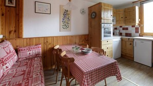 Una habitación acogedora de estilo cabaña con paredes de madera, una mesa de comedor con mantel a cuadros y una kitchenette con armarios de madera y un ventanal.