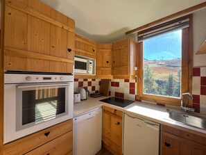 A kitchen with wooden cabinets, a microwave, an oven, a dishwasher, and a window with a view of a mountainous landscape.
