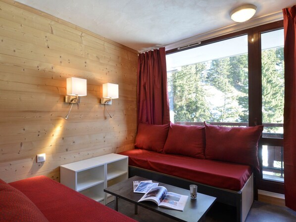 A cozy room with a wooden wall, a red sofa, a small table with a magazine, and two wall-mounted lamps.