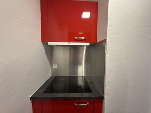 A kitchen with a stainless steel range hood, red cabinets, and a black countertop.