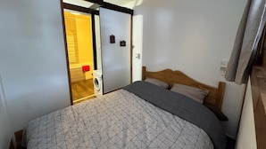 A bedroom with a bed, a washing machine, and a door leading to a bathroom. - Renovated studio in Chantemerle with parking and pets allowed (Saint-Chaffrey)