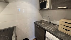 A modern kitchen with white tiles, a stainless steel sink, a microwave, and a dishwasher. - Renovated studio in Chantemerle with parking and pets allowed (Saint-Chaffrey)