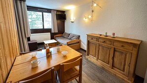 A cozy room with a wooden dining table, chairs, a sofa, and a wooden cabinet. - Renovated studio in Chantemerle with parking and pets allowed (Saint-Chaffrey)