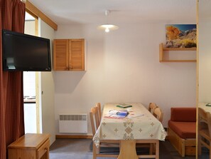 Um quarto com uma mesa de jantar, cadeiras, televisão na parede, janela com cortinas e um quadro na parede.