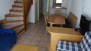 A living room with a wooden staircase, a dining table with chairs, a sofa, and a television.