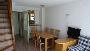A compact living space with a dining table, chairs, a sofa, a TV, and a staircase.