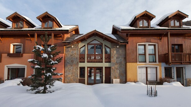 A multi-story wooden building with a stone facade, a balcony, and snow-covered surroundings.
