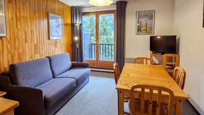 A cozy living room with a sofa, a wooden dining table, and a TV. - Cozy studio in Flaine, south balcony, near slopes (Flaine)