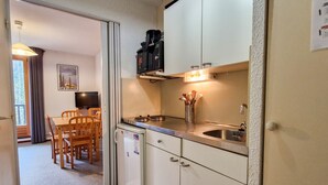 A compact kitchen with a microwave, stove, and sink. There is a dining area with a table and chairs. - Cozy studio in Flaine, south balcony, near slopes (Flaine)