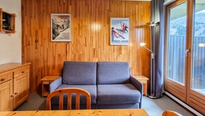 A cozy room with a wooden wall, a grey sofa, a wooden table, and a window with a view of a snowy landscape. - Cozy studio in Flaine, south balcony, near slopes (Flaine)