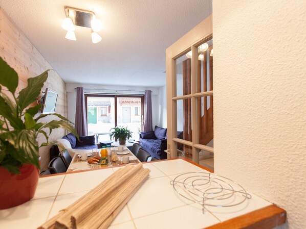 A cozy room with a dining table, chairs, a plant, and a view of the outside through a window.
