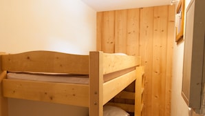 A bunk bed with a wooden headboard and mattress, set against a wooden wall with a small window.
