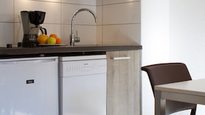 A kitchen with a dishwasher, a coffee maker, and a sink with a faucet. There are oranges on the counter.