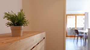 A wooden dresser with a potted plant, a white wall, and a glimpse of a dining area with chairs and a table.