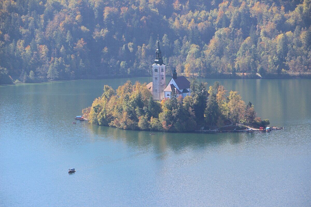 A small island with a church and a tower surrounded by a forested lake.