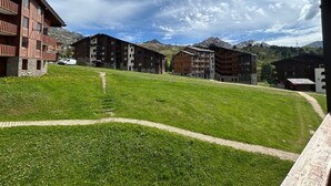 A hotel with multiple buildings, a grassy courtyard, and mountains in the background. - Comfortable 2-room apartment, direct slope access, sleeps 6 (Belle Plagne)