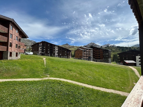 Un hotel con varias construcciones, un patio cubierto de césped y montañas al fondo.
