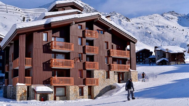 A multi-story wooden building with balconies, set against a snowy mountain backdrop. - Comfortable 2-room apartment, direct slope access, sleeps 6 (Belle Plagne)