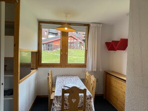 A dining area with a table and chairs, a window with a view of buildings, and a red wall decoration. - Comfortable 2-room apartment, direct slope access, sleeps 6 (Belle Plagne)