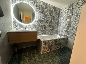 A bathroom with a sink, mirror, and bathtub.