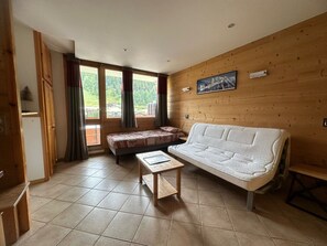 A cozy room with a sofa, a small table, and a window offering a view of a mountainous landscape.