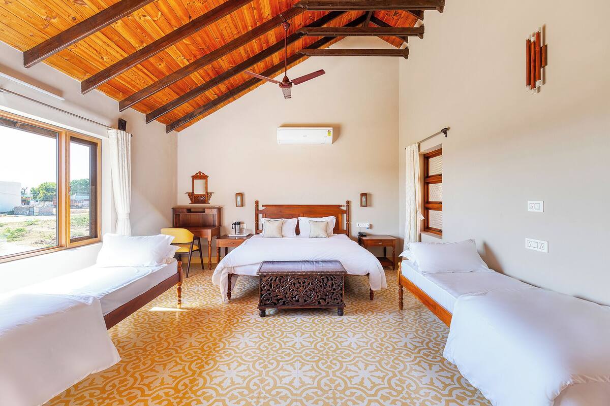 A hotel room with a large bed, two single beds, a wooden ceiling, a window, and a patterned floor.