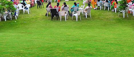 Um grupo de pessoas sentadas em círculo em um campo gramado com cadeiras brancas, cercadas por árvores.