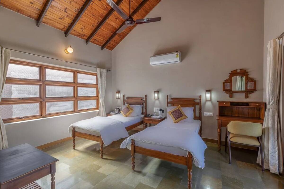 A room with two wooden beds, a desk, a chair, and a ceiling fan.