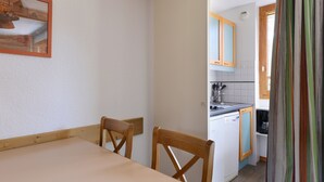 Un coin repas avec une table et des chaises, une cuisine équipée de placards et d’un évier, et une fenêtre avec des rideaux.
