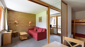 Une pièce avec un mur en bois, un canapé rouge, une table en bois, un petit bureau et un lit superposé.