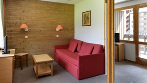 Une pièce de taille modeste avec un mur en bois, un canapé rouge, une petite table en bois et deux lampes fixées au mur.