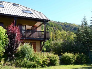 A two-story building with a balcony, surrounded by lush greenery and hills in the background.