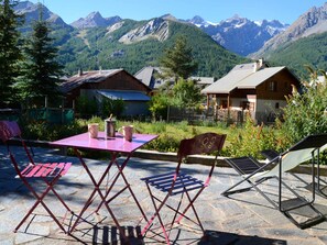 A patio with a table and chairs, surrounded by mountains and wooden buildings.
