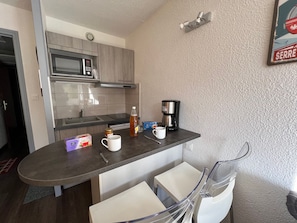 A compact kitchen with a microwave, coffee maker, and a small table with chairs.